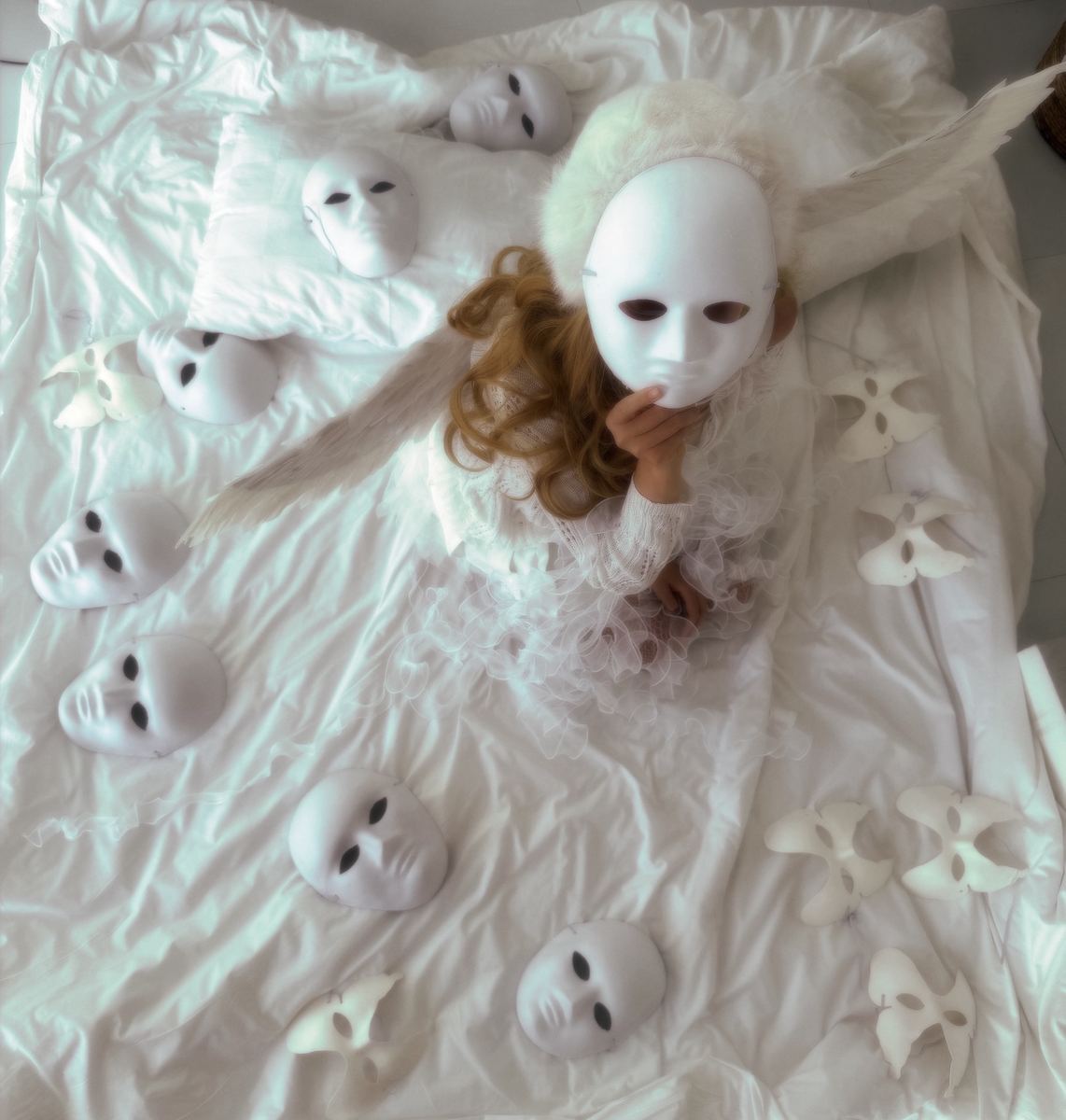 Masked angel figure in white surrounded by cast blank faces and paper birds